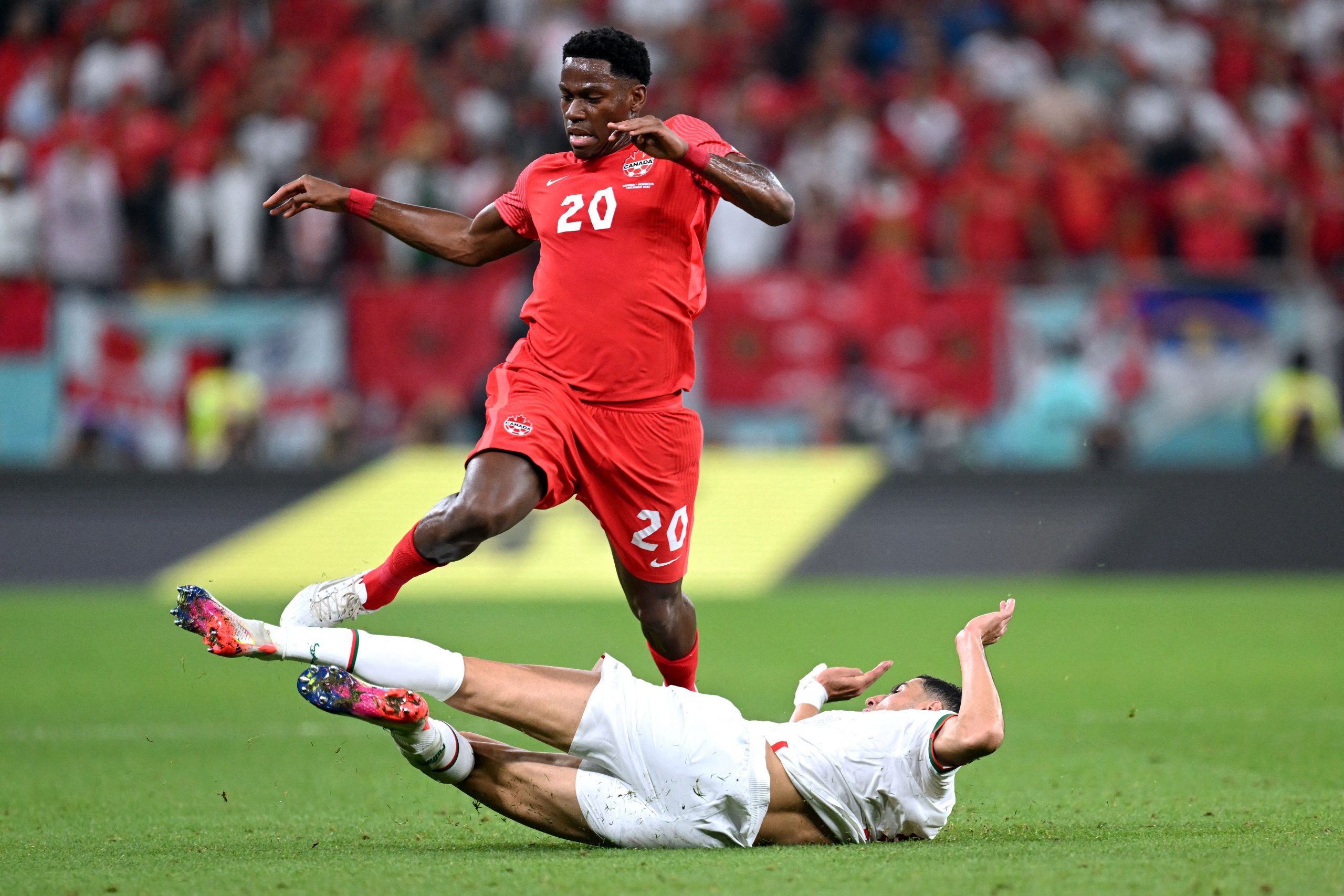 Canada's forward #20 Jonathan David (top) jumps over a Morocco player during the Qatar 2022 World Cup Group F football match between Canada and Morocco at the Al-Thumama Stadium in Doha on December 1, 2022